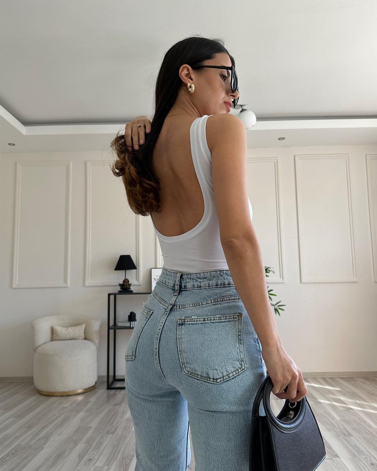 Woman wearing a white low-back bodysuit and light blue high-waisted denim jeans.