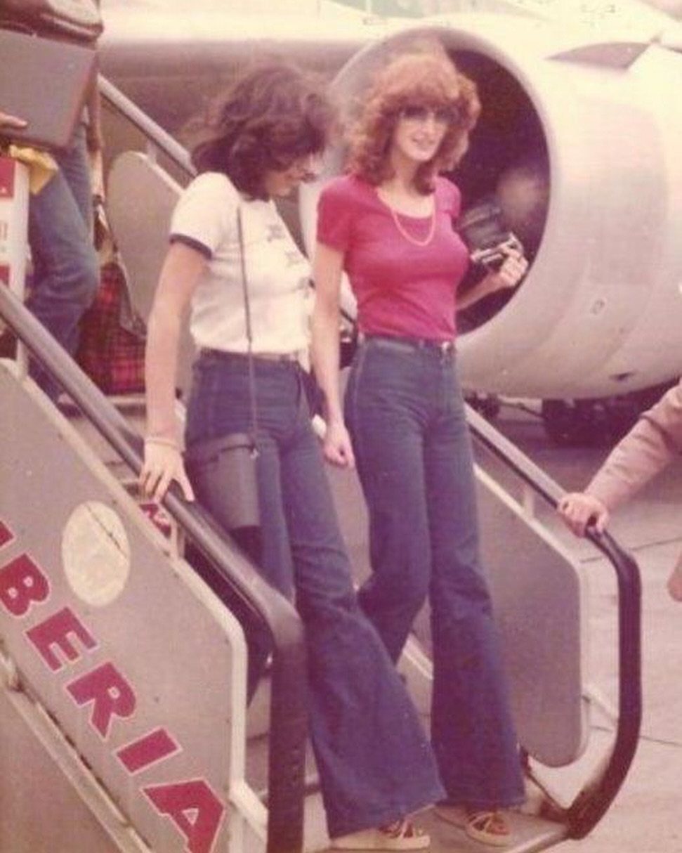 Two women in flared denim jeans walking down the stairs of an airplane.