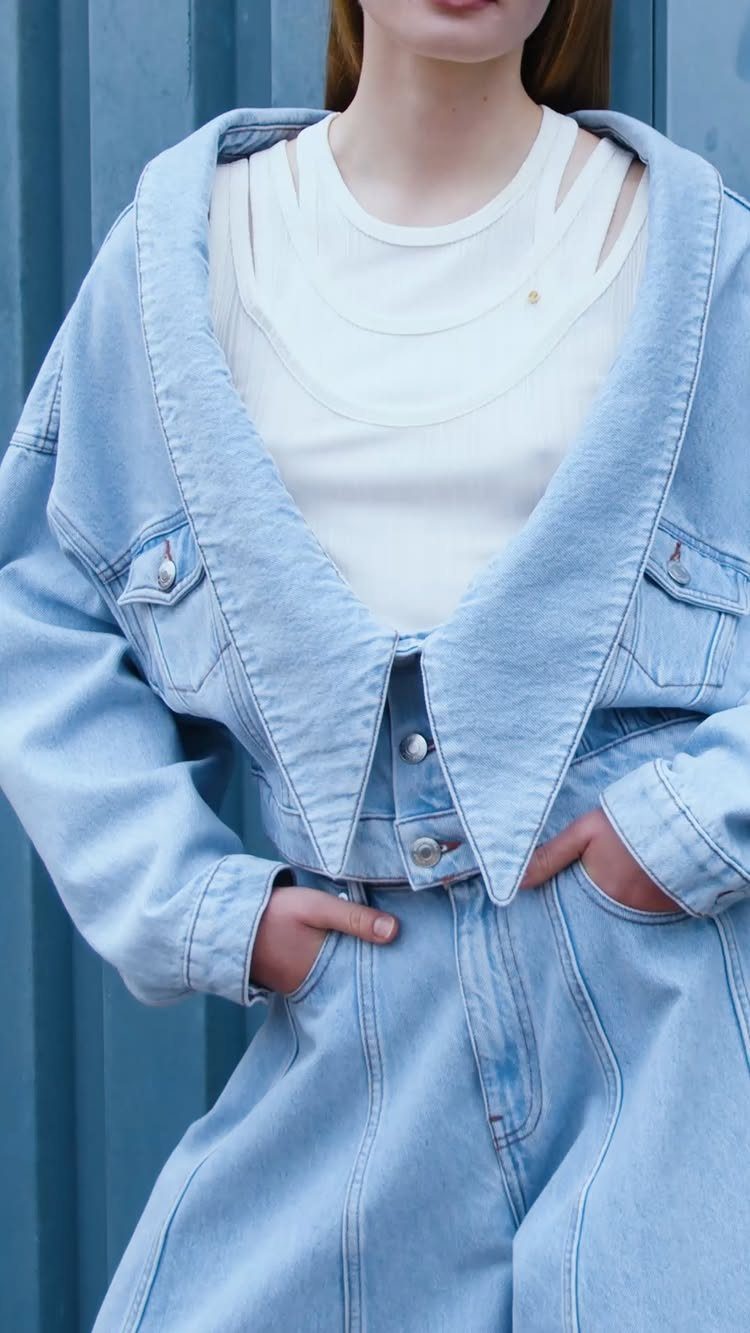 A person wearing a light blue denim jacket and matching high waisted denim pants.