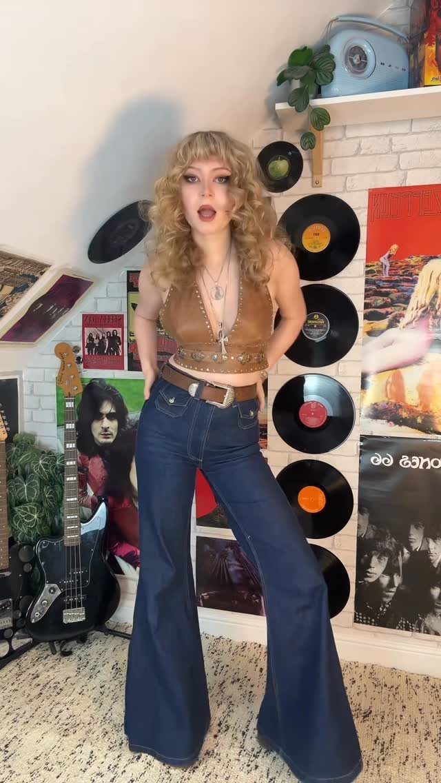 Woman posing in a brown leather top and dark blue high waisted flare jeans.