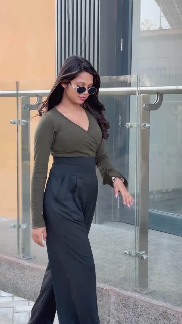 A woman walking in an olive green wrap top and black high waisted wide-leg pants.