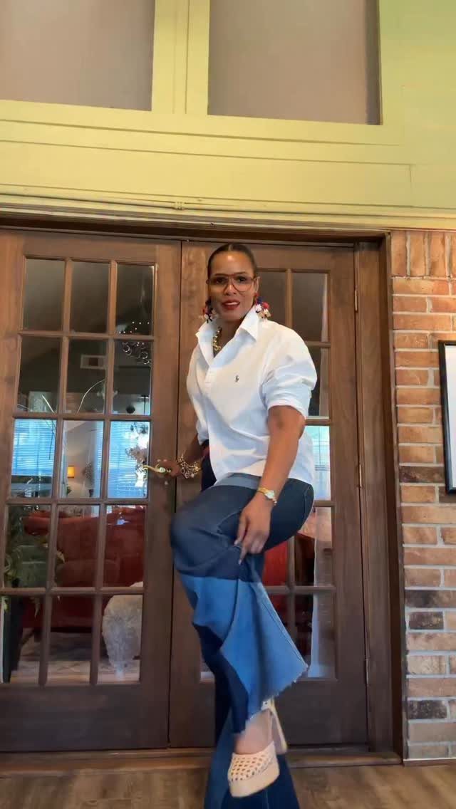 A woman posing in a white shirt and stylishly paneled blue denim trousers.