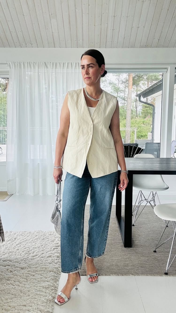Woman wearing blue denim jeans, a cream vest, and silver strappy high heels.
