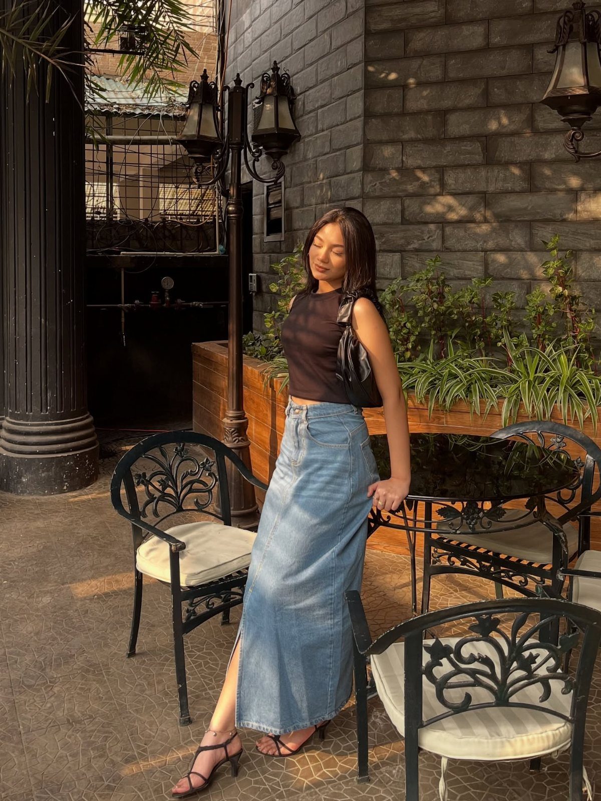 A woman posing in a black top and a long denim maxi skirt outdoors.