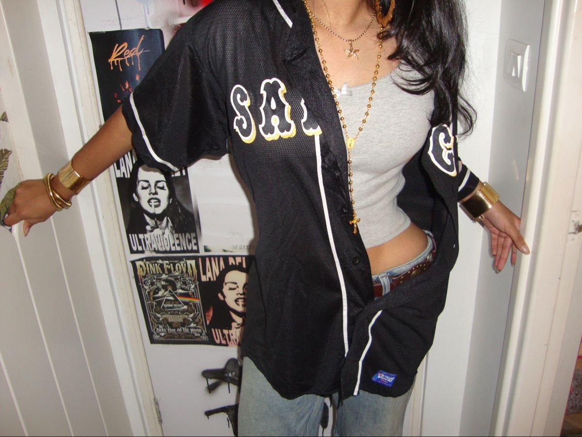 Woman wearing an oversized black baseball jersey over a grey tank top and blue jeans.