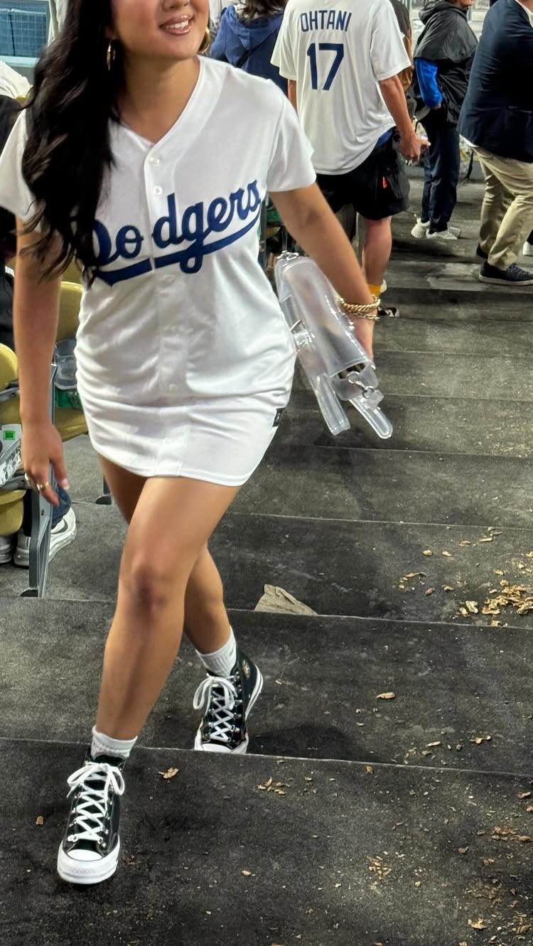 A woman walking down stairs wearing a white Dodgers jersey styled as a dress with black sneakers.
