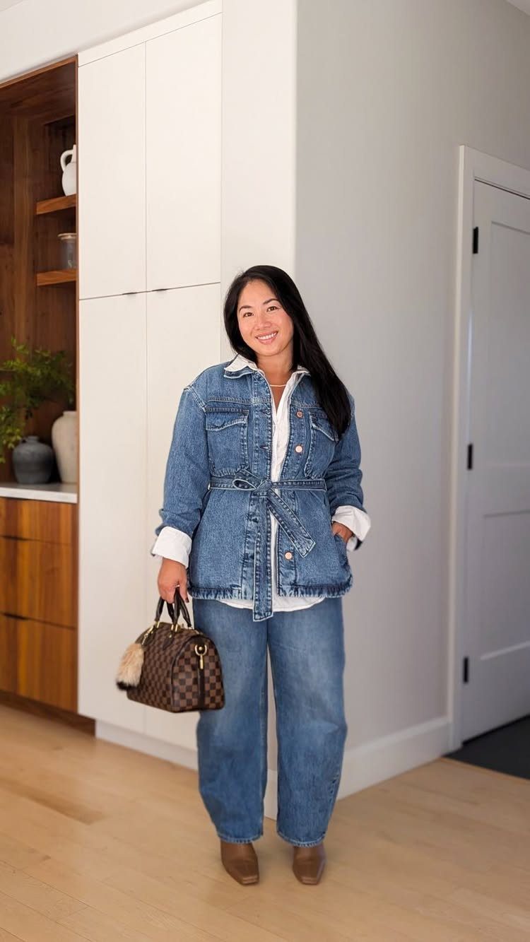 Woman wearing a belted denim jacket and wide-leg jeans while holding a handbag.