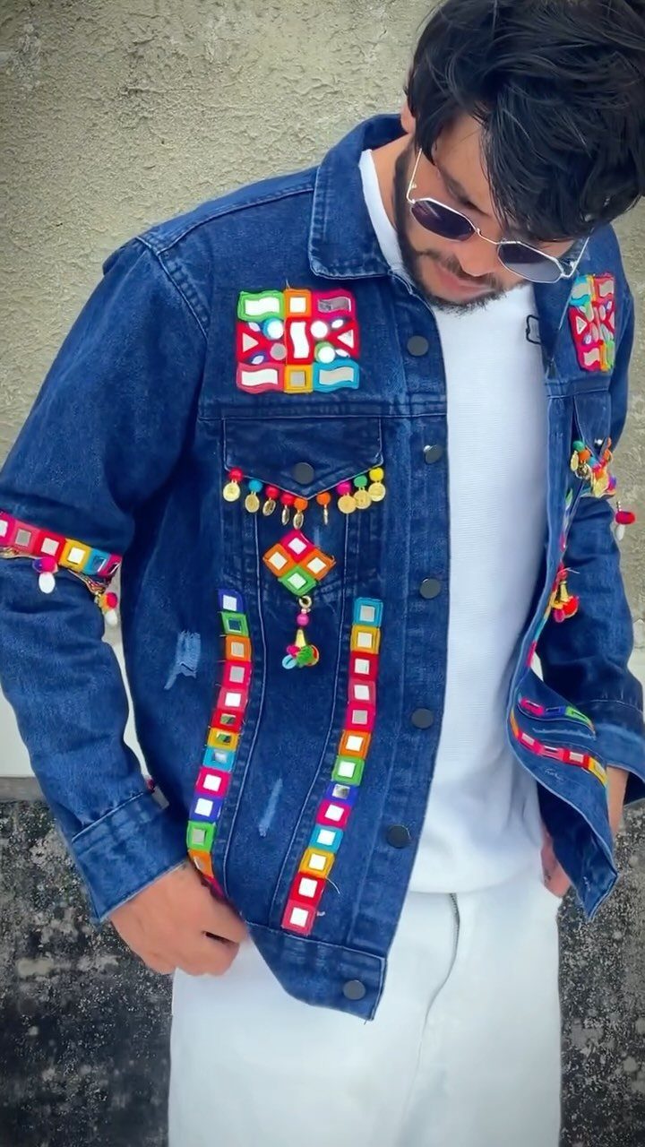 Man wearing a blue denim jacket with colorful geometric patches and hanging charms.