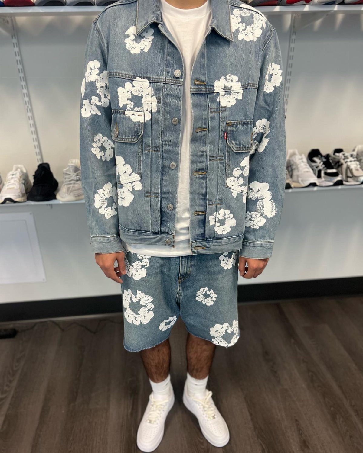 Person wearing a light wash denim jacket and shorts with white floral patterns.