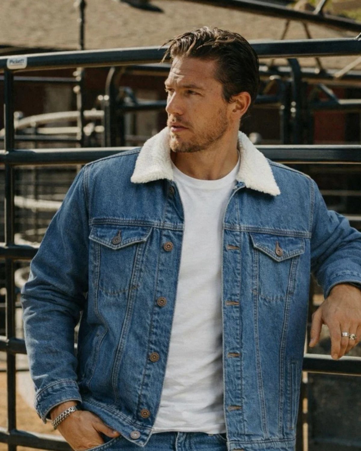 A man in a blue denim jacket with a white sherpa collar and white t-shirt.