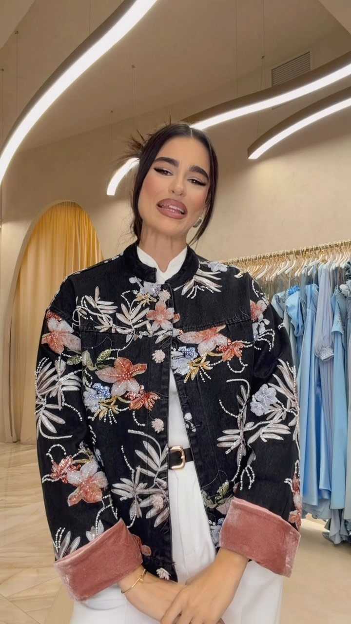 Woman wearing a black denim jacket with vibrant, large-scale floral embroidery.