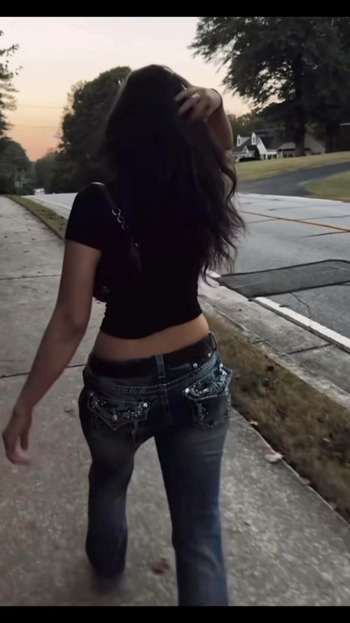 Woman walking on a sidewalk wearing a black crop top and dark blue denim jeans.
