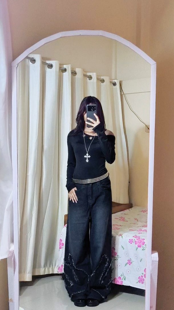 Woman in black top and wide-leg dark jeans posing for a mirror selfie.