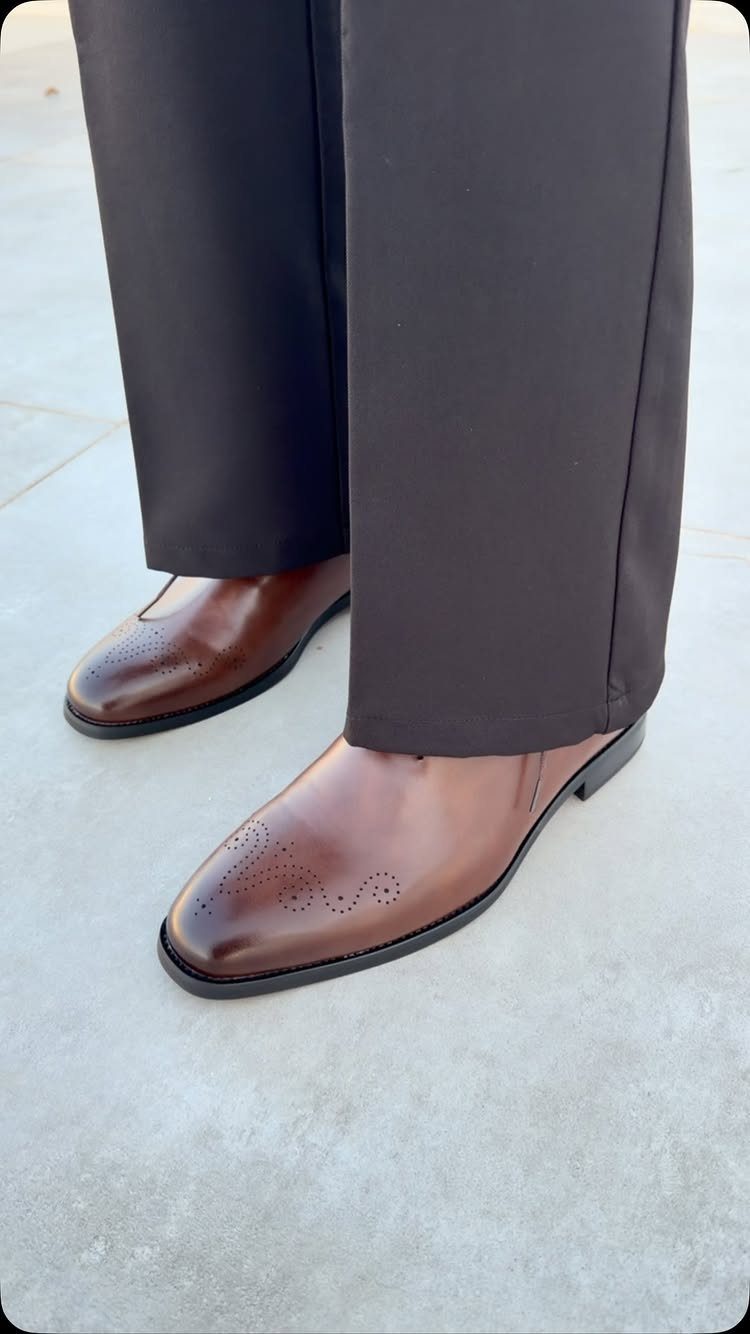 Brown leather brogue dress shoes worn with dark trousers on concrete.