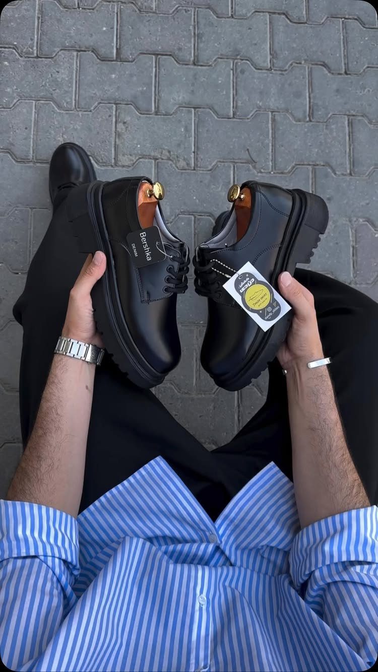 A person holding a pair of black leather derby shoes with thick soles.