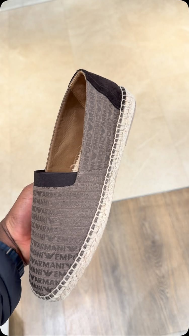 A grey patterned Armani slip-on espadrille with a braided rope sole held by a hand.