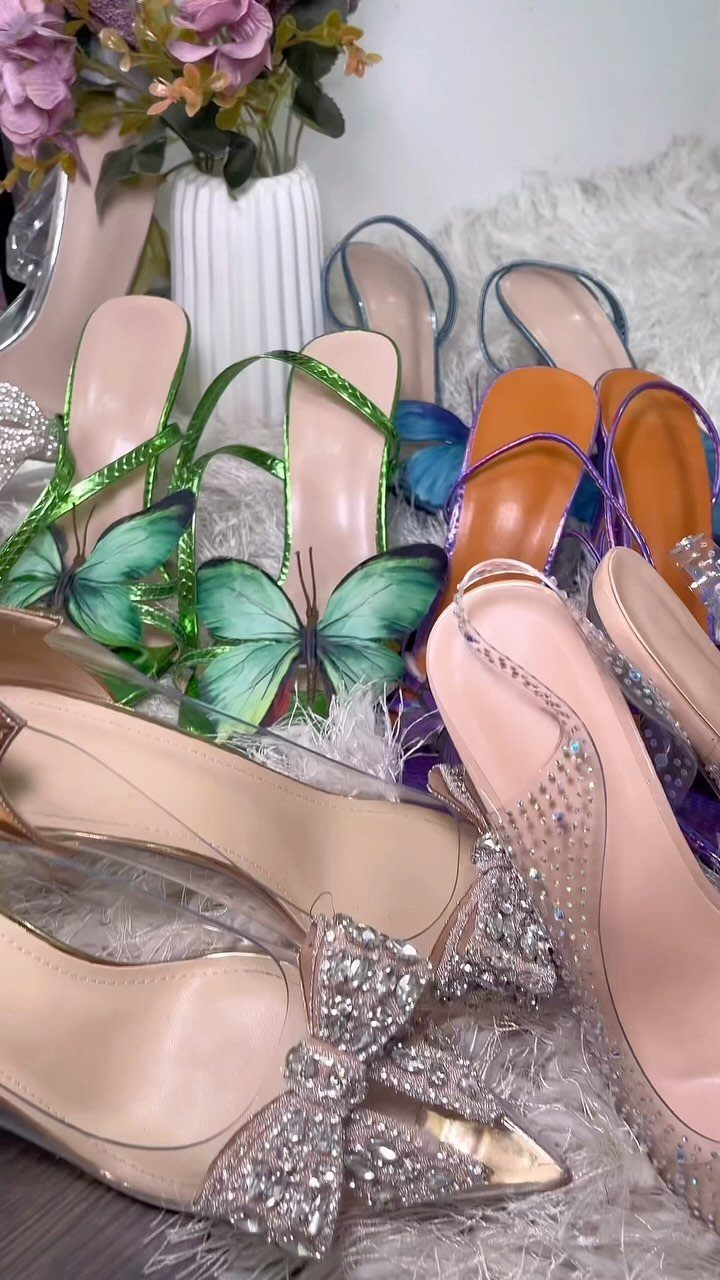 Various colorful women's high-heeled sandals and rhinestone-decorated pumps on a white fuzzy surface.