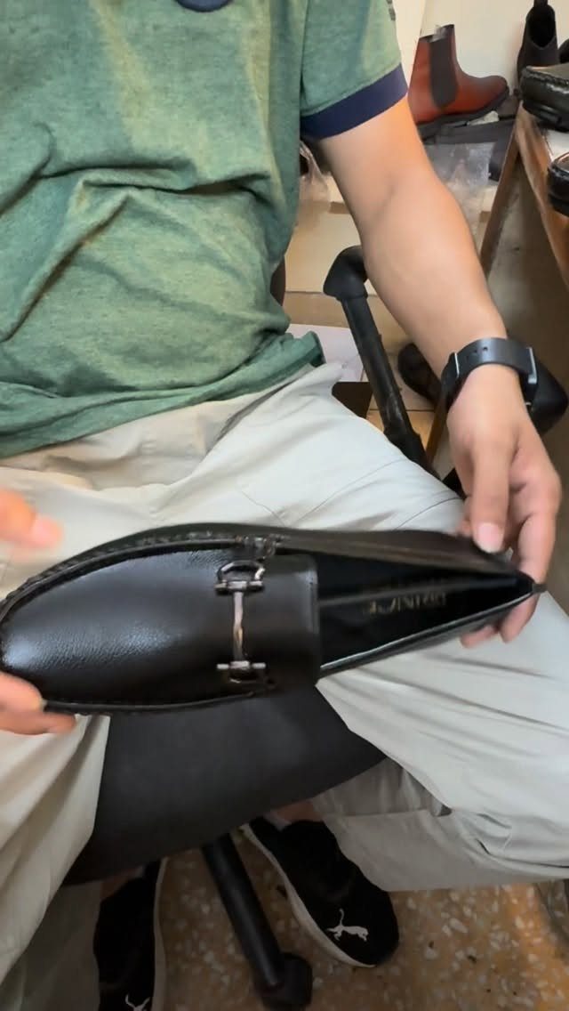 A person holding a pair of black leather loafers with silver metal hardware.