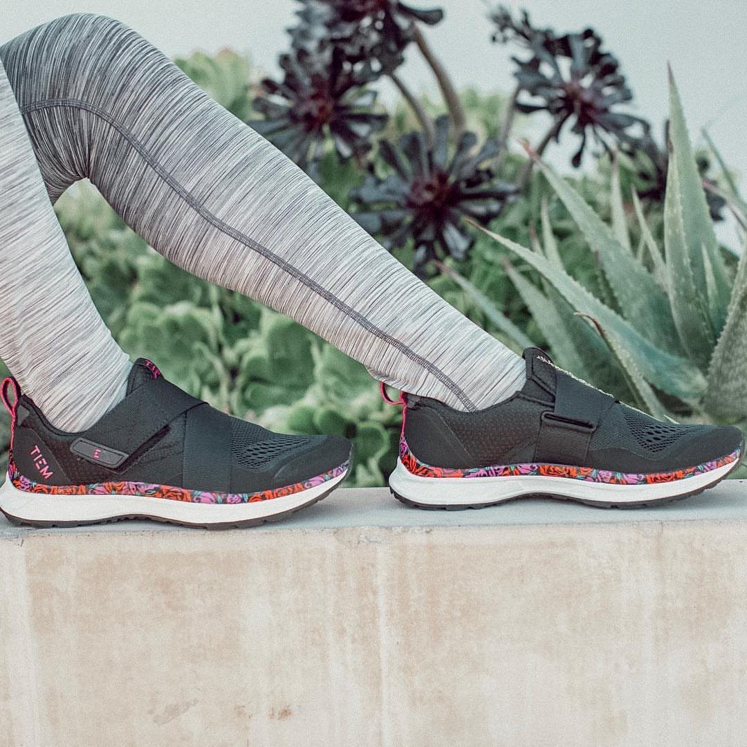 Black athletic sneakers with patterned soles worn by a person in grey leggings.