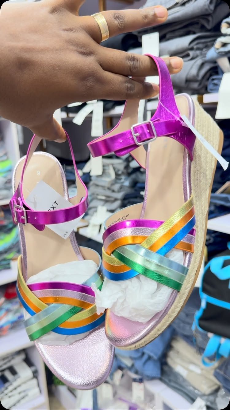 Pink rainbow wedge sandals held up by a hand in a clothing store.