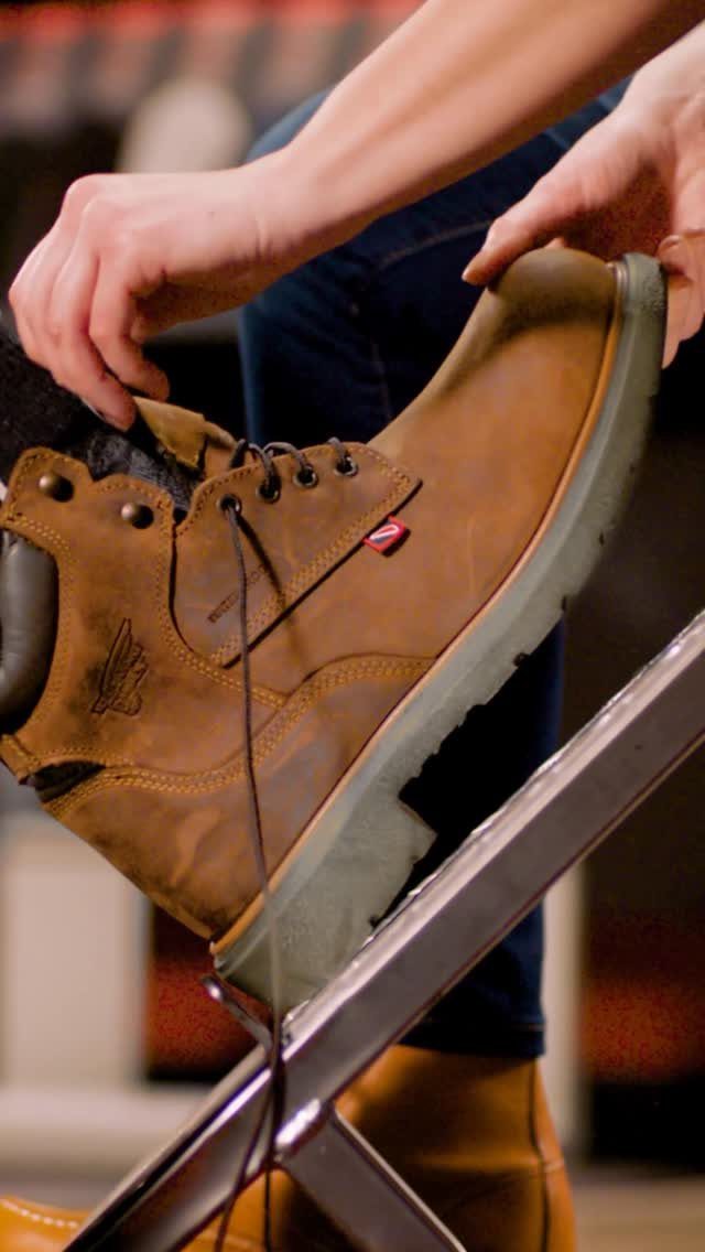 A person holding a sturdy brown leather work boot with thick soles.