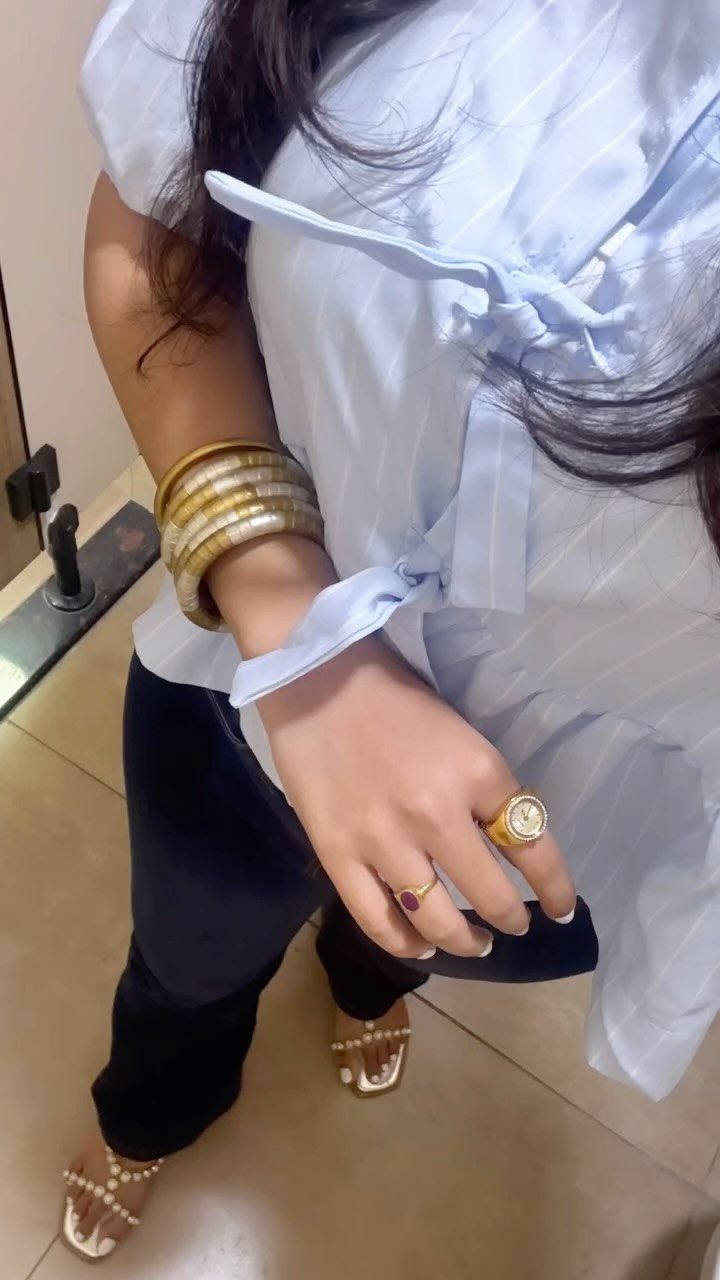 Person wearing light blue striped shirt, gold bangles, and a gold ring.