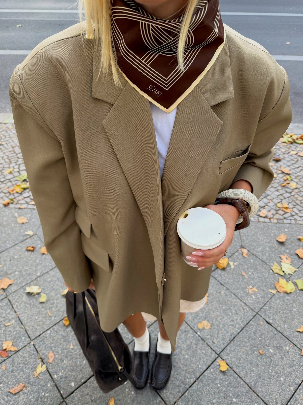 A person wearing an oversized tan blazer, white t-shirt, and a patterned brown neck scarf.