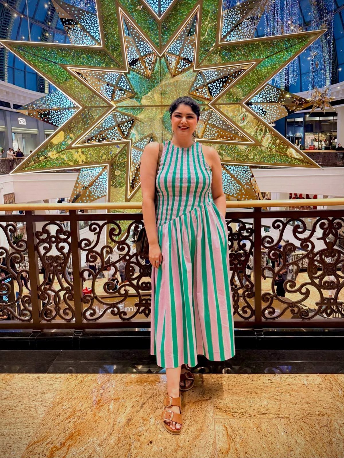 A woman wearing a pink and green striped maxi dress standing in a mall.