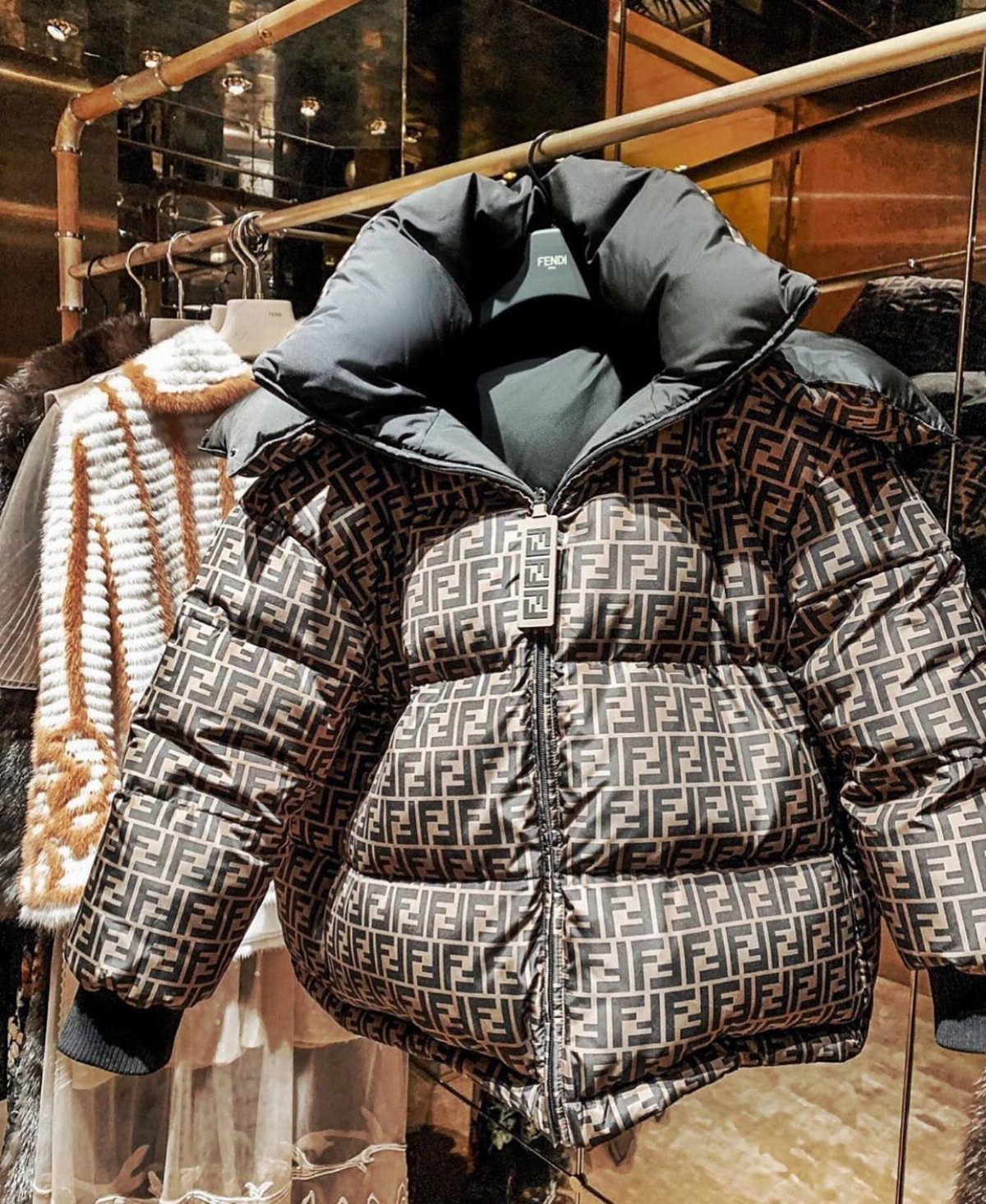 A Fendi monogram puffer jacket hanging on a gold clothing rack in a luxury boutique.