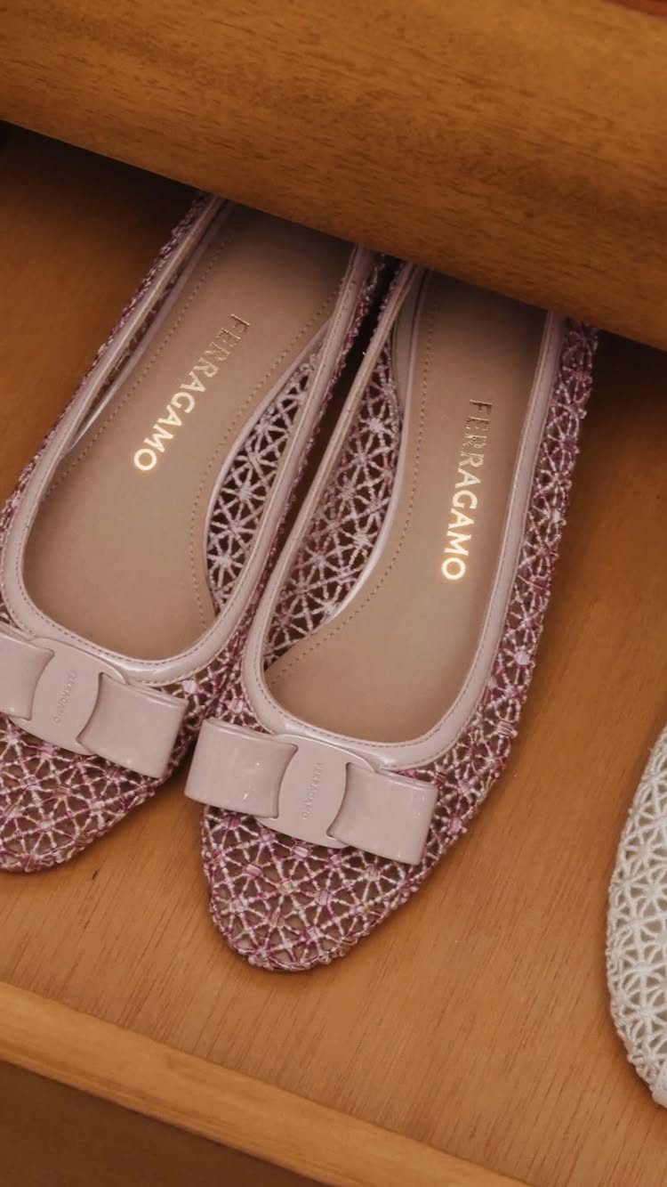 Pink Ferragamo mesh ballet flats with bows sitting inside a wooden drawer.