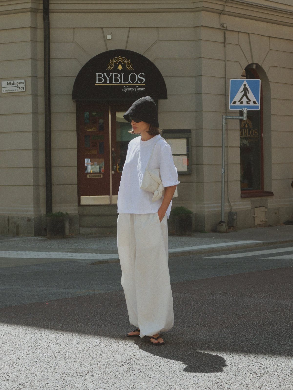 Woman in white minimalist clothing and a black beret standing on a city street.