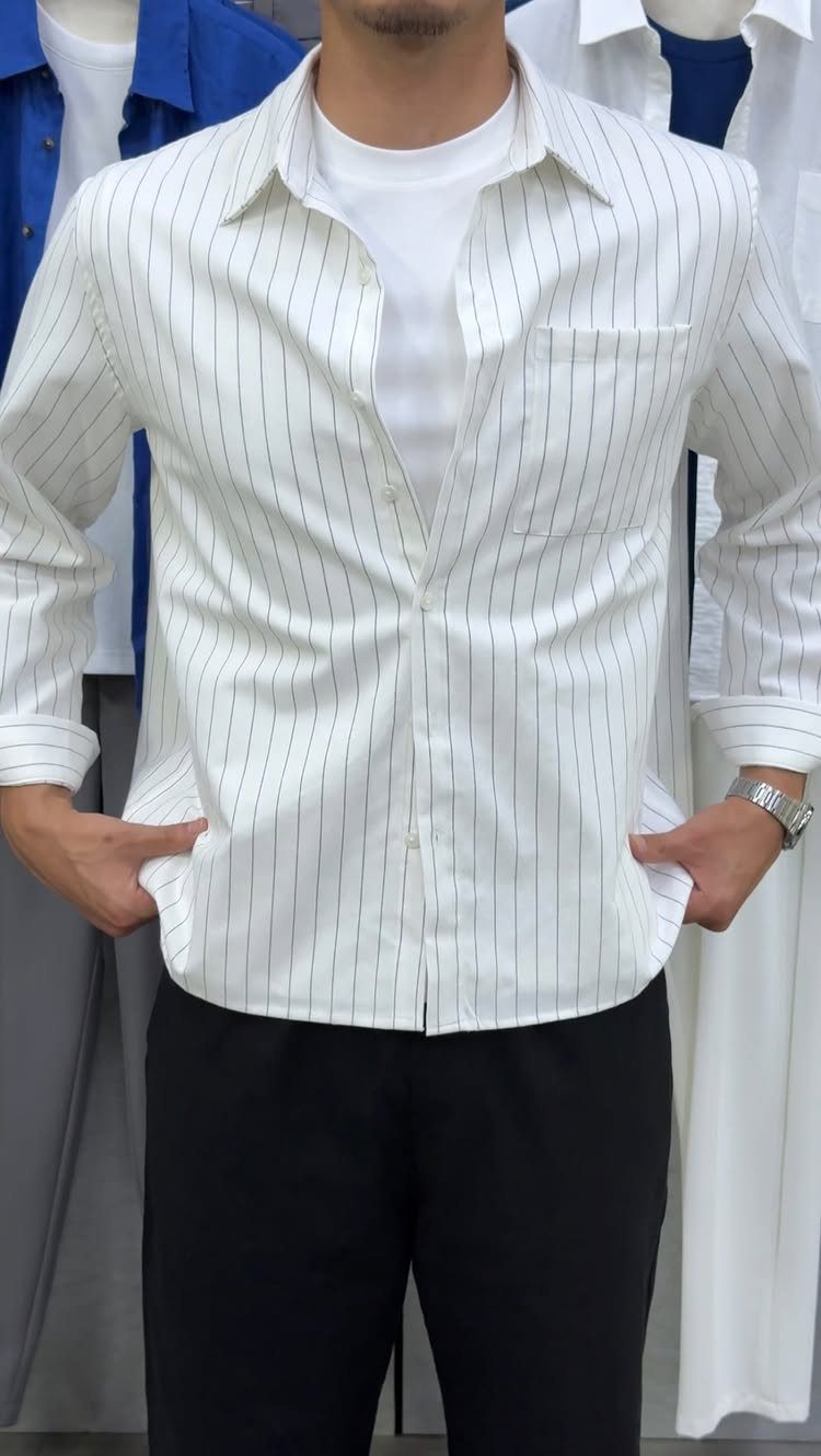 A person wearing a striped white shirt over a white t-shirt and black pants.