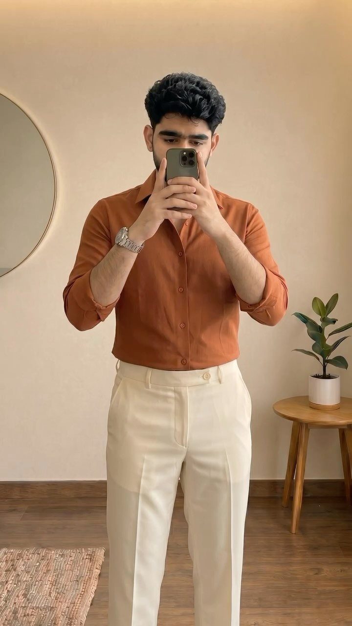 Man in orange shirt and cream trousers posing for a mirror selfie.