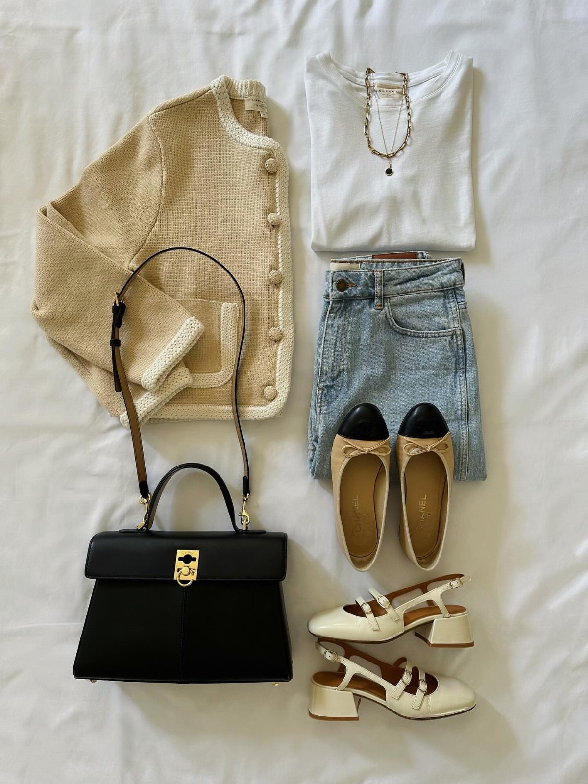 Beige cardigan, white t-shirt, blue jeans, black handbag, and various shoes laid out on a white background.