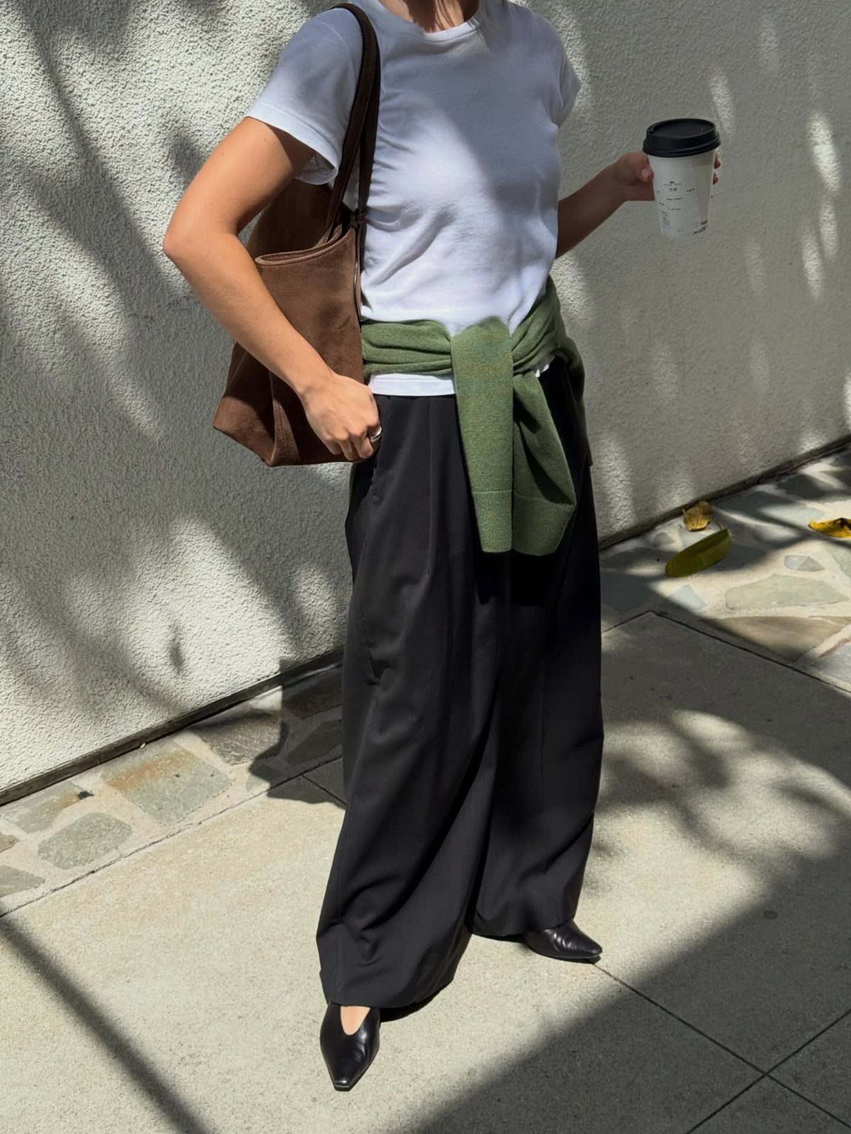 Person wearing a white t-shirt, black wide-leg trousers, and a green sweater tied around their waist.