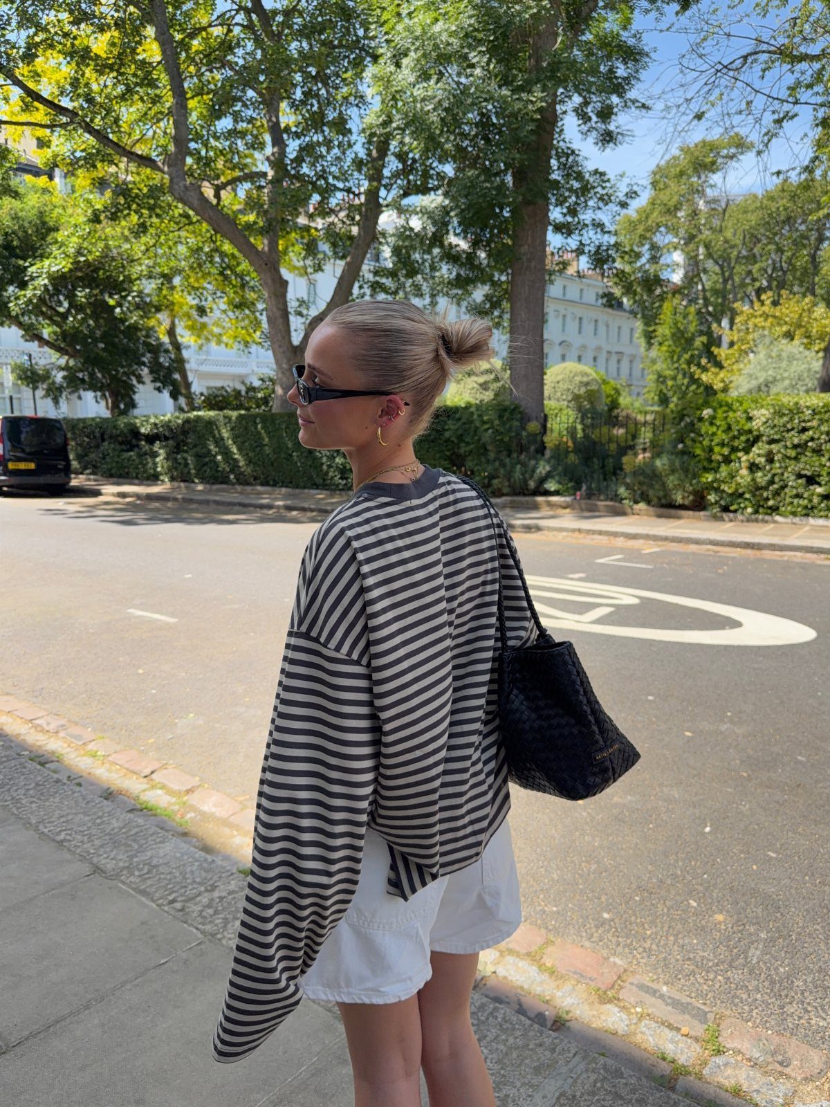 Woman in an oversized striped tunic and white shorts walking on a sunny city street.