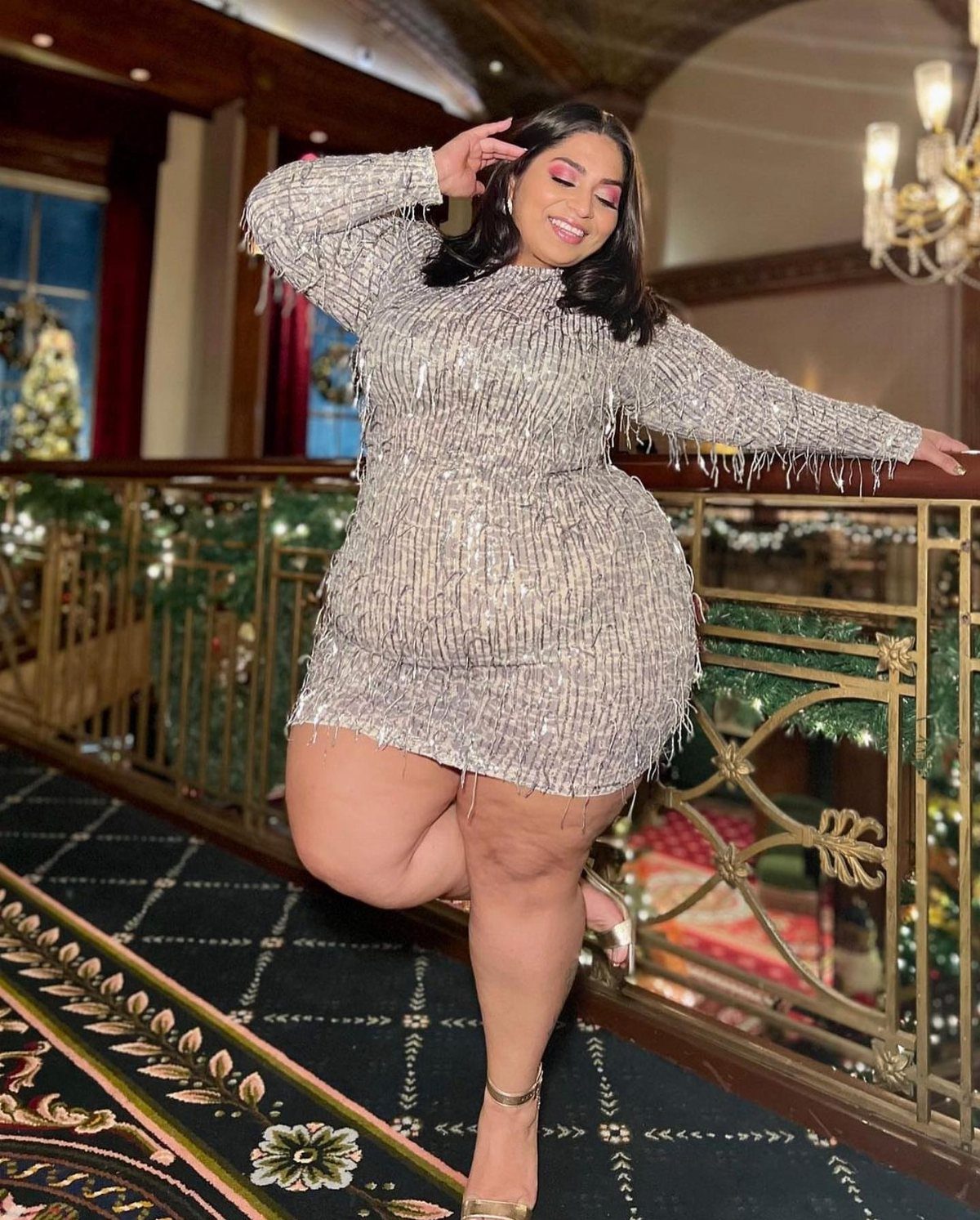A woman smiling while posing in a shimmering silver sequined mini dress with fringe.