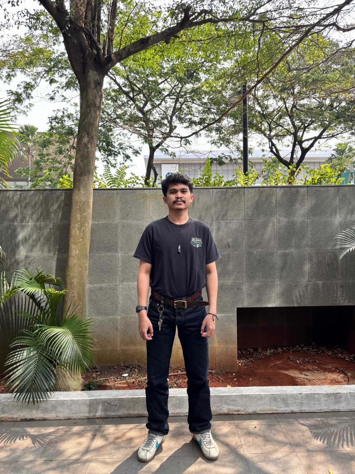 Man wearing a black graphic t-shirt, dark denim jeans, and white Nike Cortez sneakers.