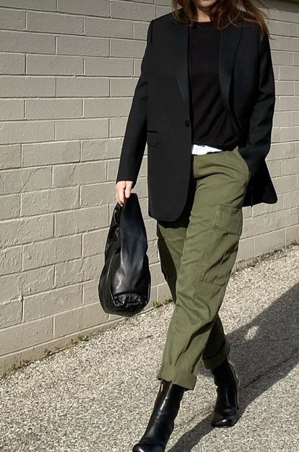 Person wearing a black blazer, black top, olive green cargo pants, and black boots walking outdoors.