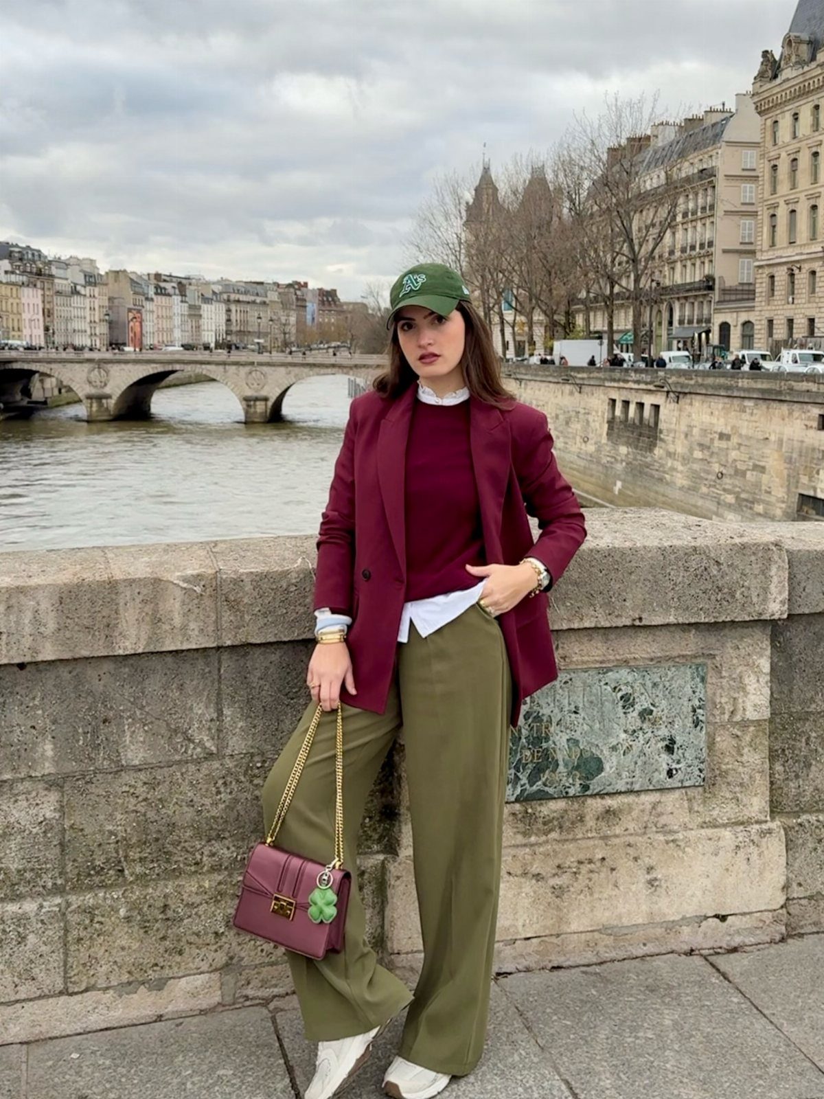 Woman wearing a burgundy blazer, burgundy sweater, and wide-leg olive green pants by a river.