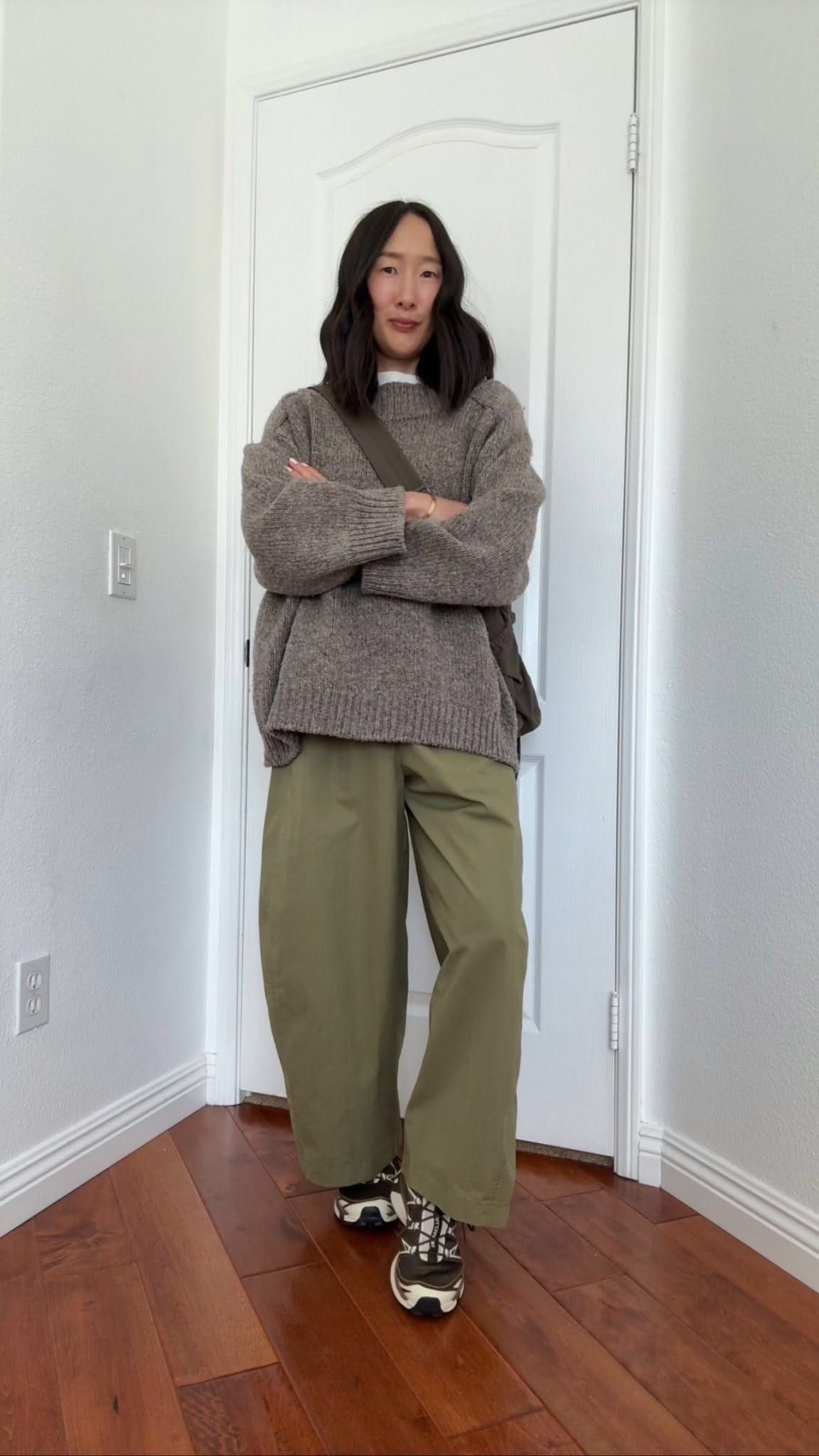 Woman wearing wide-leg olive green pants and a chunky brown knit sweater standing indoors.