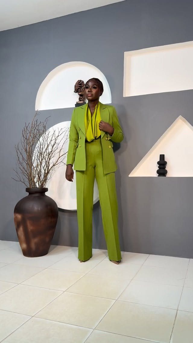 Woman posing in a bright lime green blazer and matching wide-leg trousers against a grey wall.