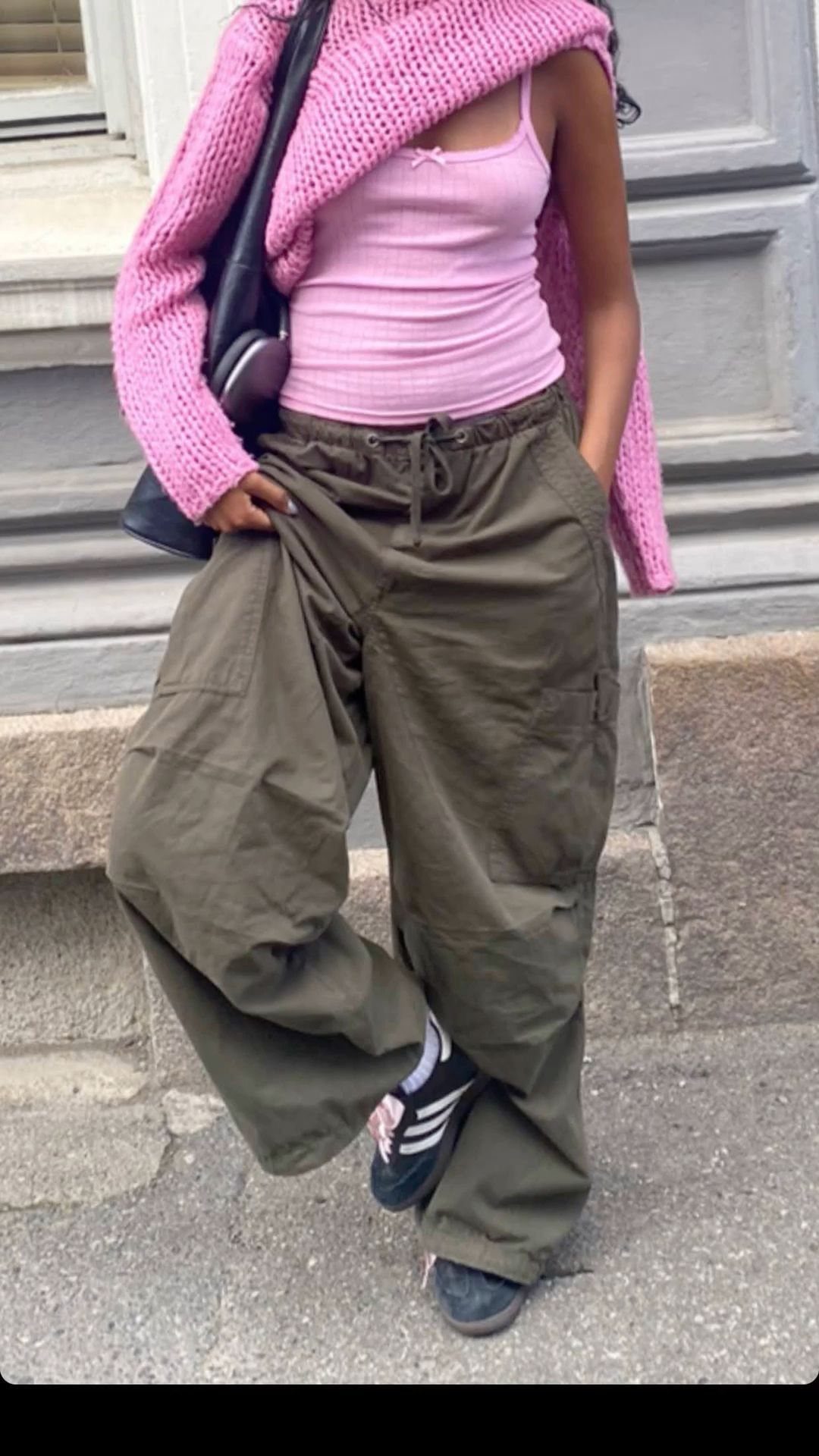 Person wearing olive green cargo pants with a pink tank top and bright pink cardigan.