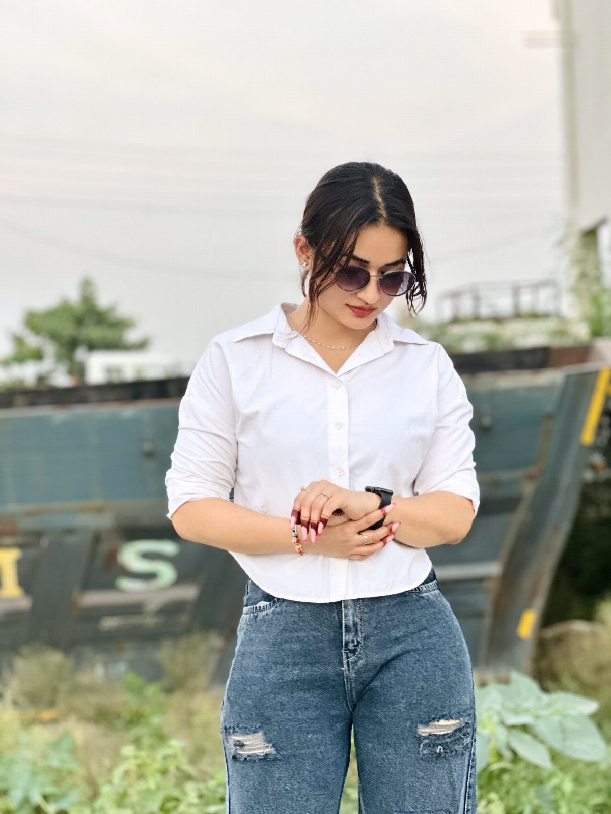 A woman posing in a white button-down shirt and blue ripped jeans outdoors.