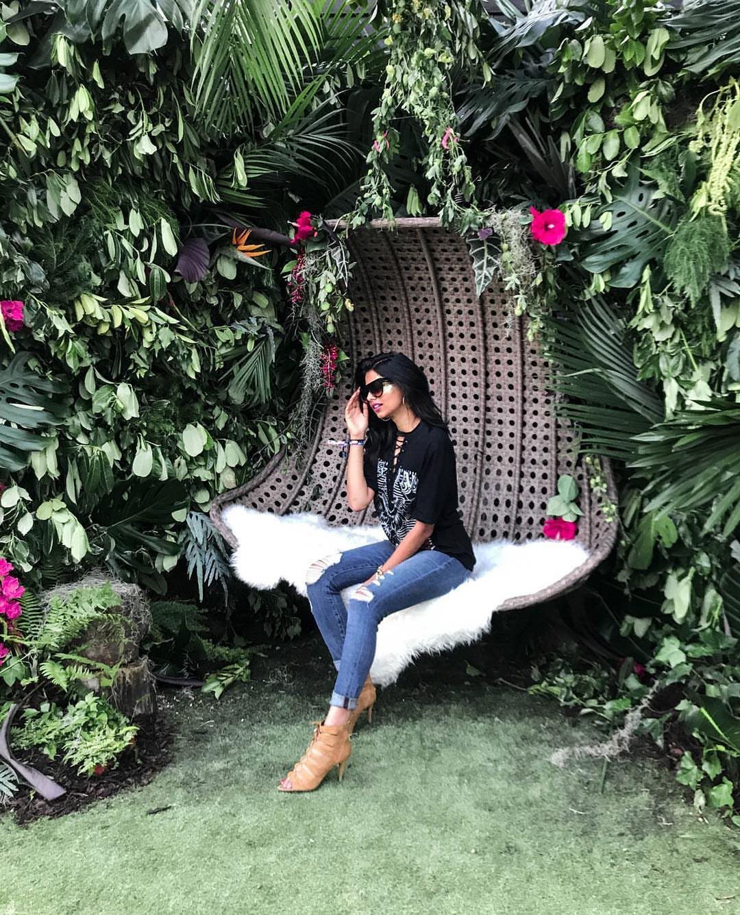 Woman in a black graphic tee and ripped jeans sitting on a wicker swing chair.