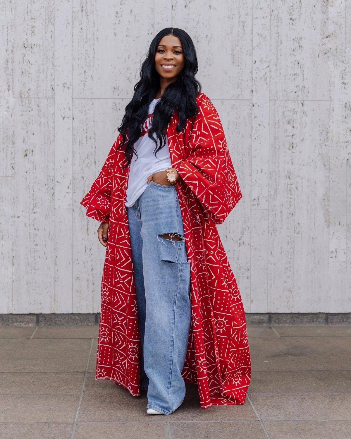 Woman smiling in a red patterned kimono, white t-shirt, and light blue ripped jeans.