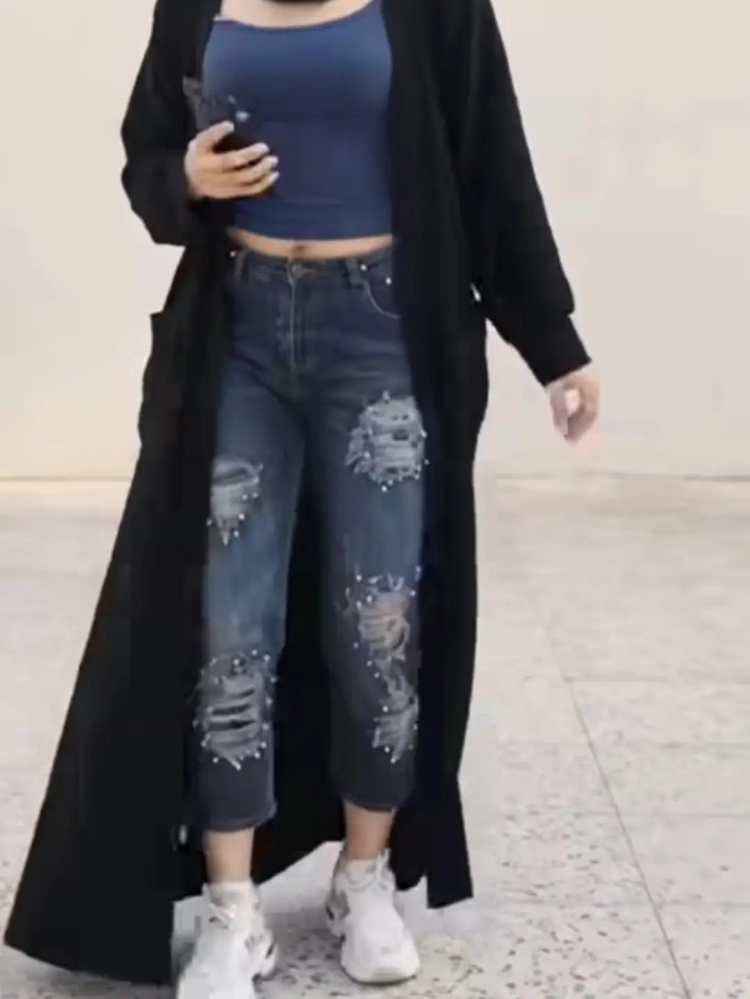 Person wearing pearl-embellished ripped jeans, a blue top, and a long black cardigan.