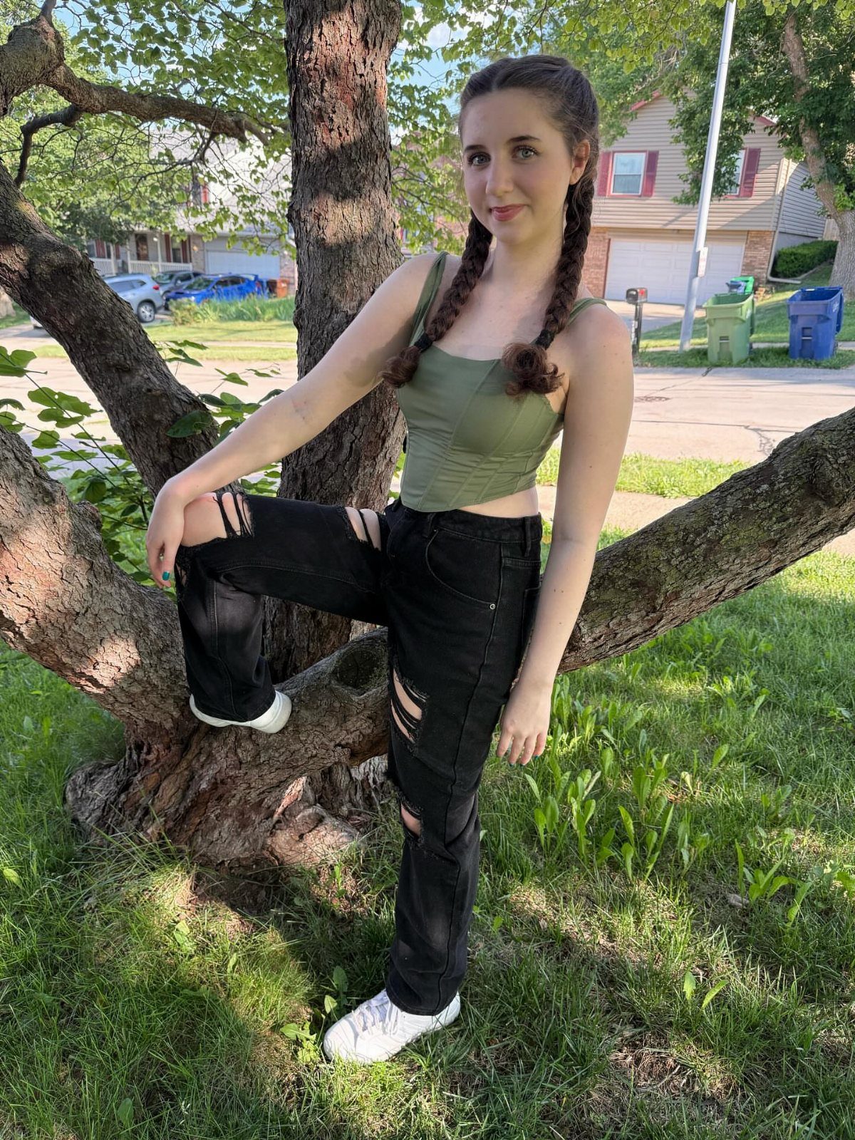 A woman wearing black ripped jeans and a green structured crop top posing by a tree.