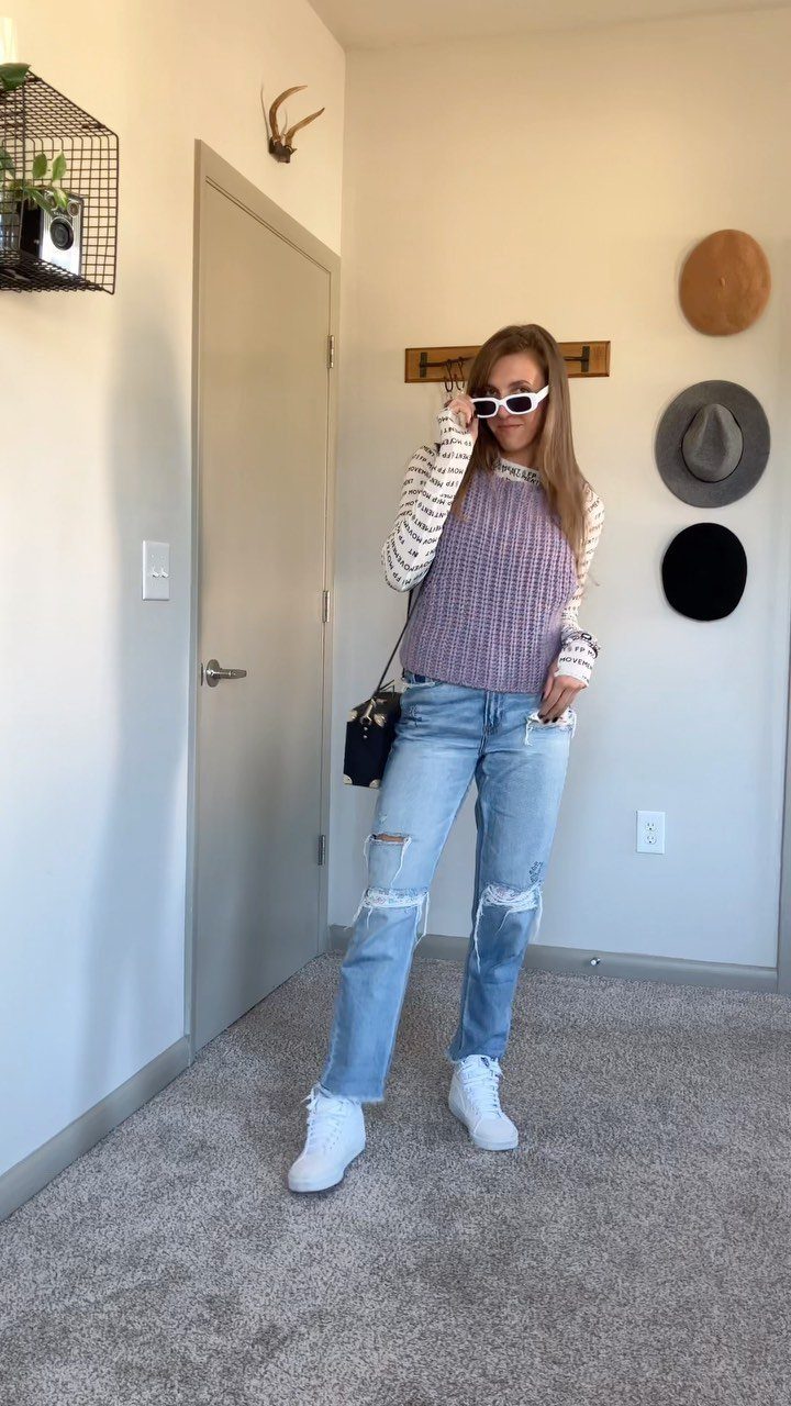 Woman posing in light blue ripped jeans, a purple sweater vest, and white sneakers.