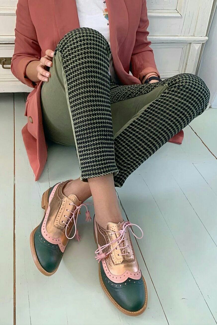 Person wearing colorful wingtip oxford shoes, houndstooth trousers, and a coral blazer sitting on a floor.